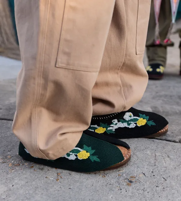 A person with brown pants is wearing the Denim Tears Tasman.