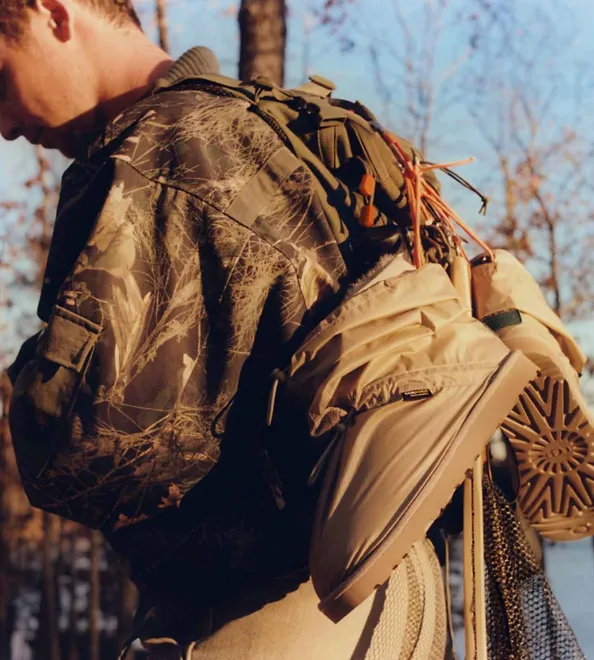 A man by the lake carrying UGG Reese Cooper boots on his back.