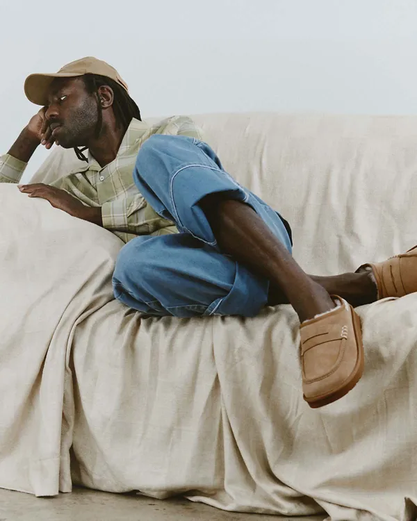 A man sitting on a couch wearing our UGG JW Anderson Loafer.