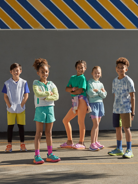 Group of children standing wearing HOKA shoes.