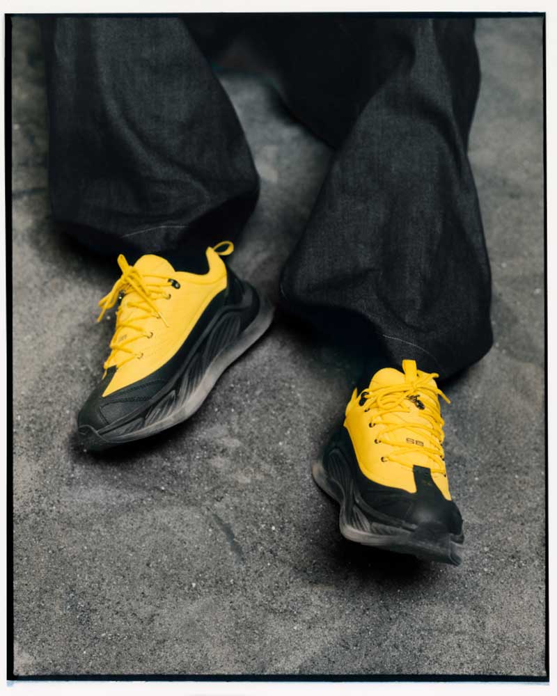 Modèle portant des chaussures Hoka x Spencer Badu avec un gros plan sur le côté de la chaussure.