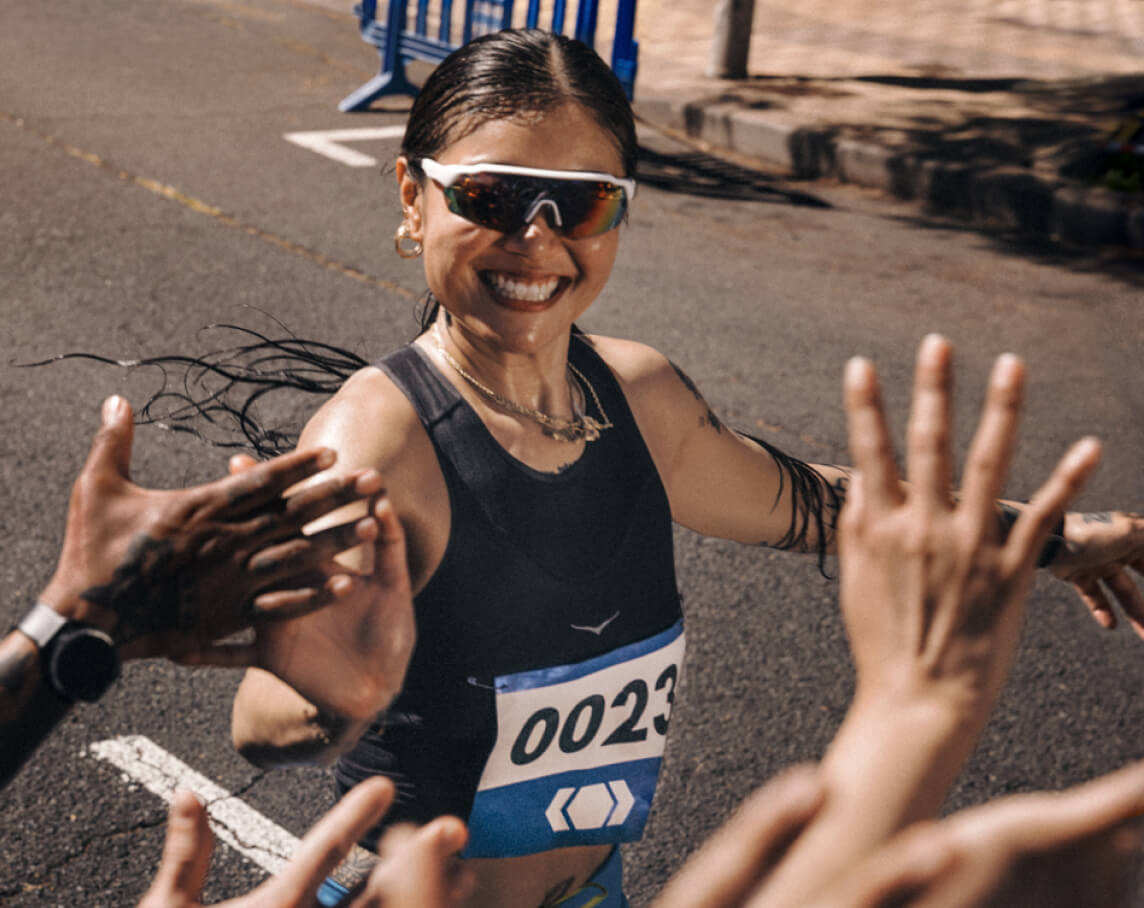 Un coureur en tenue HOKA tape dans les mains de la foule avec un grand sourire pendant une course.