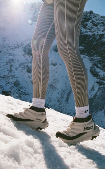 Gros plan des jambes d’une personne marchant sur la neige et portant des chaussures HOKA Kaha 2 Frost Moc GTX Halfdays.