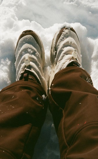 Gros plan des jambes d’une personne posées sur la neige et portant des chaussures HOKA Kaha 2 Frost Moc GTX Halfdays.