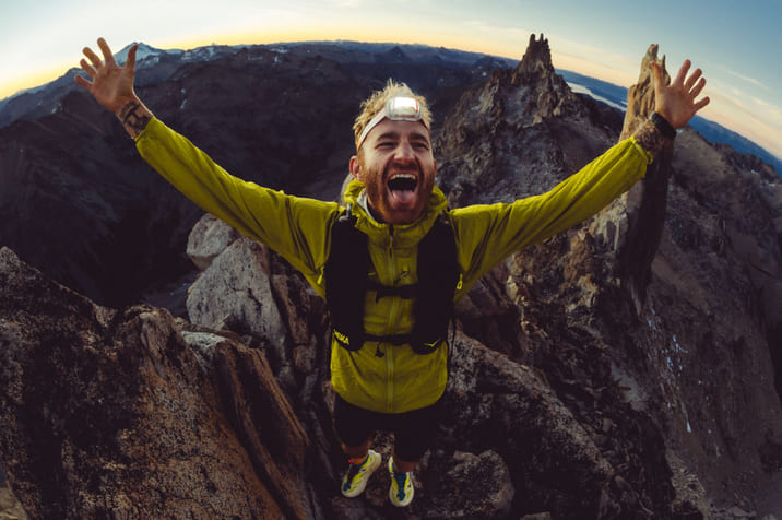 Une photo d’un homme au sommet d’une montagne, ouvrant les bras et souriant.