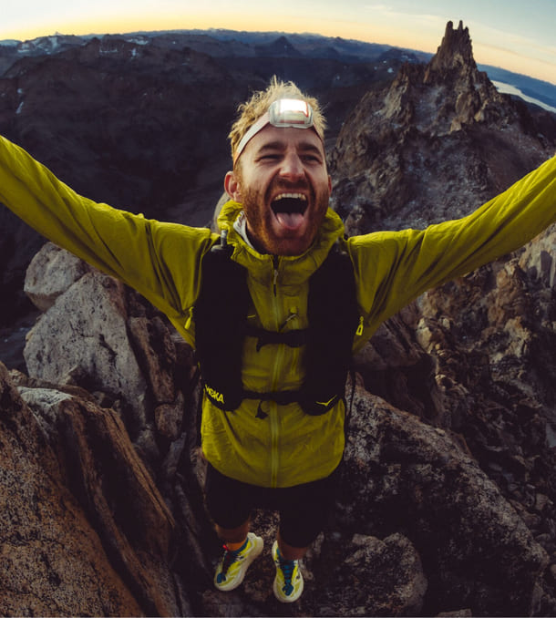 Une photo d’un homme au sommet d’une montagne, ouvrant les bras et souriant.