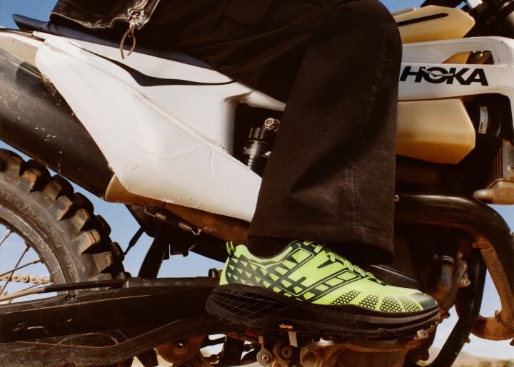 Gros plan de chaussures HOKA sur un modèle assis sur une moto.