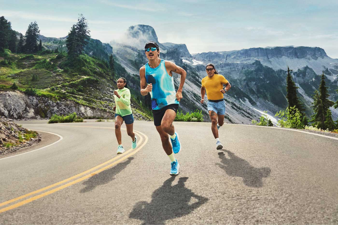 Trois personnes courant sur une route de montagne portant des équipements HOKA et des chaussures de course sur route HOKA.