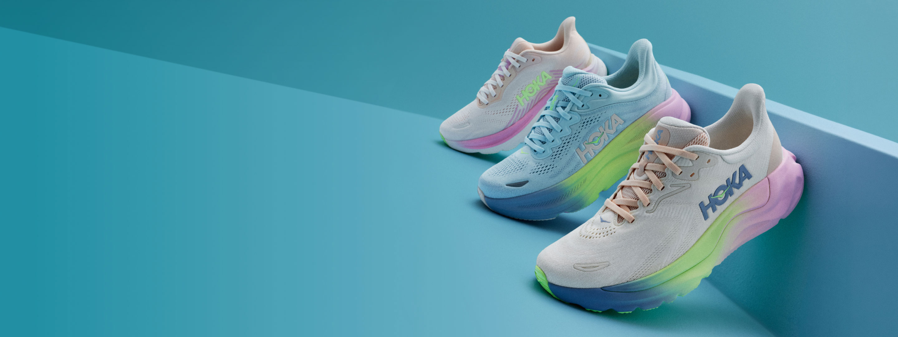 Trois chaussures HOKA appuyées contre un mur court bleu sur fond bleu.