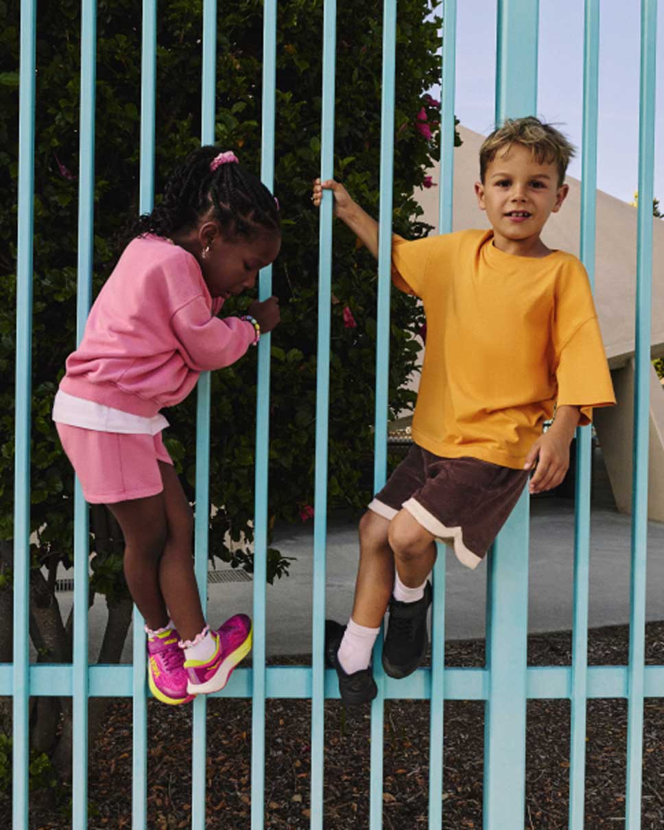 Deux enfants jouant sur une clôture en portant des chaussures HOKA.