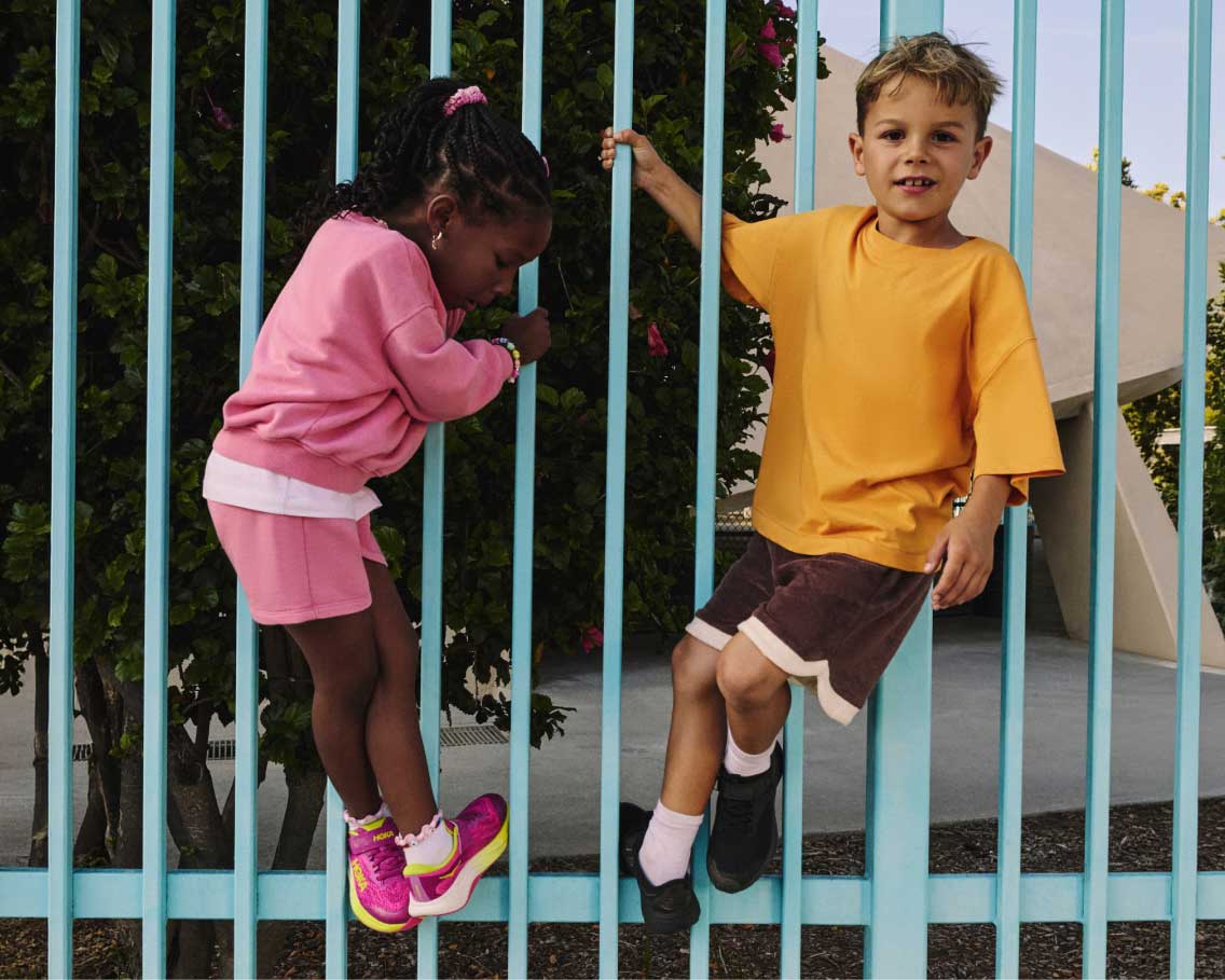 Deux enfants jouant sur une clôture en portant des chaussures HOKA.
