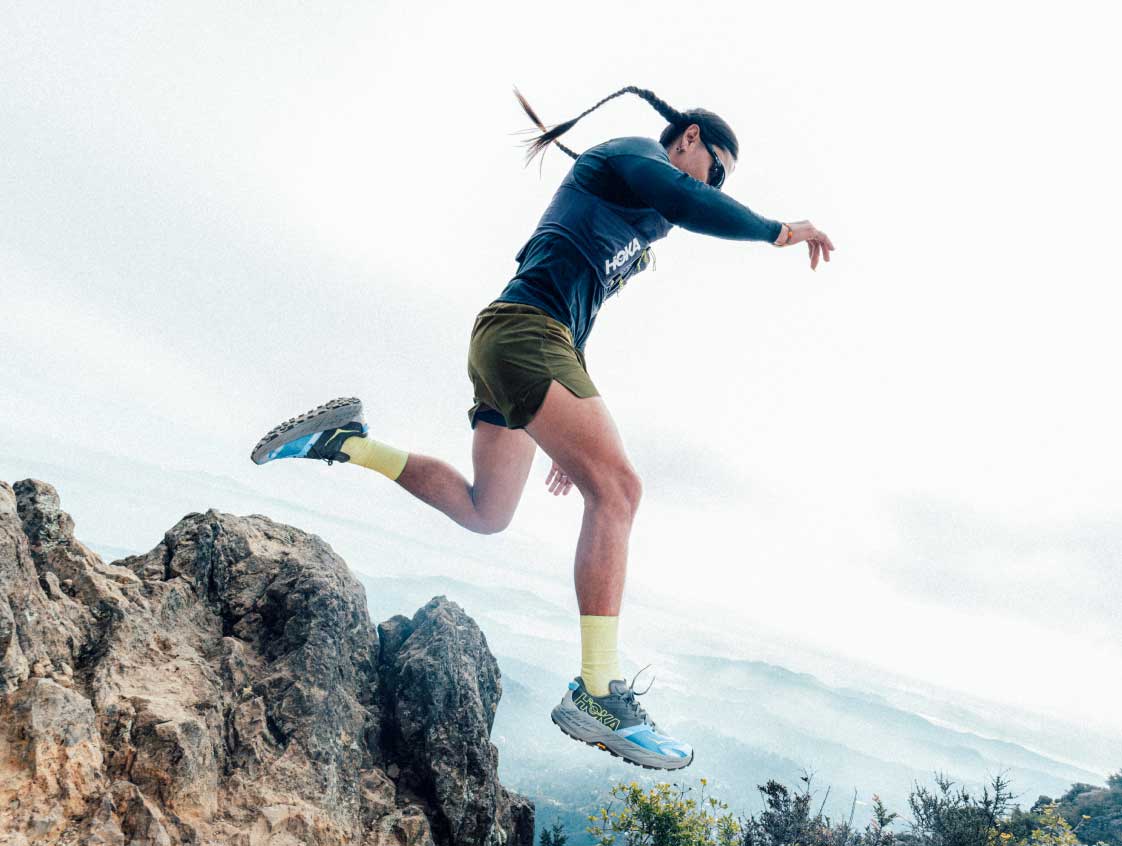 Coureur de sentier portant un Hoka Speedgoat 7 sautant par-dessus des rochers.