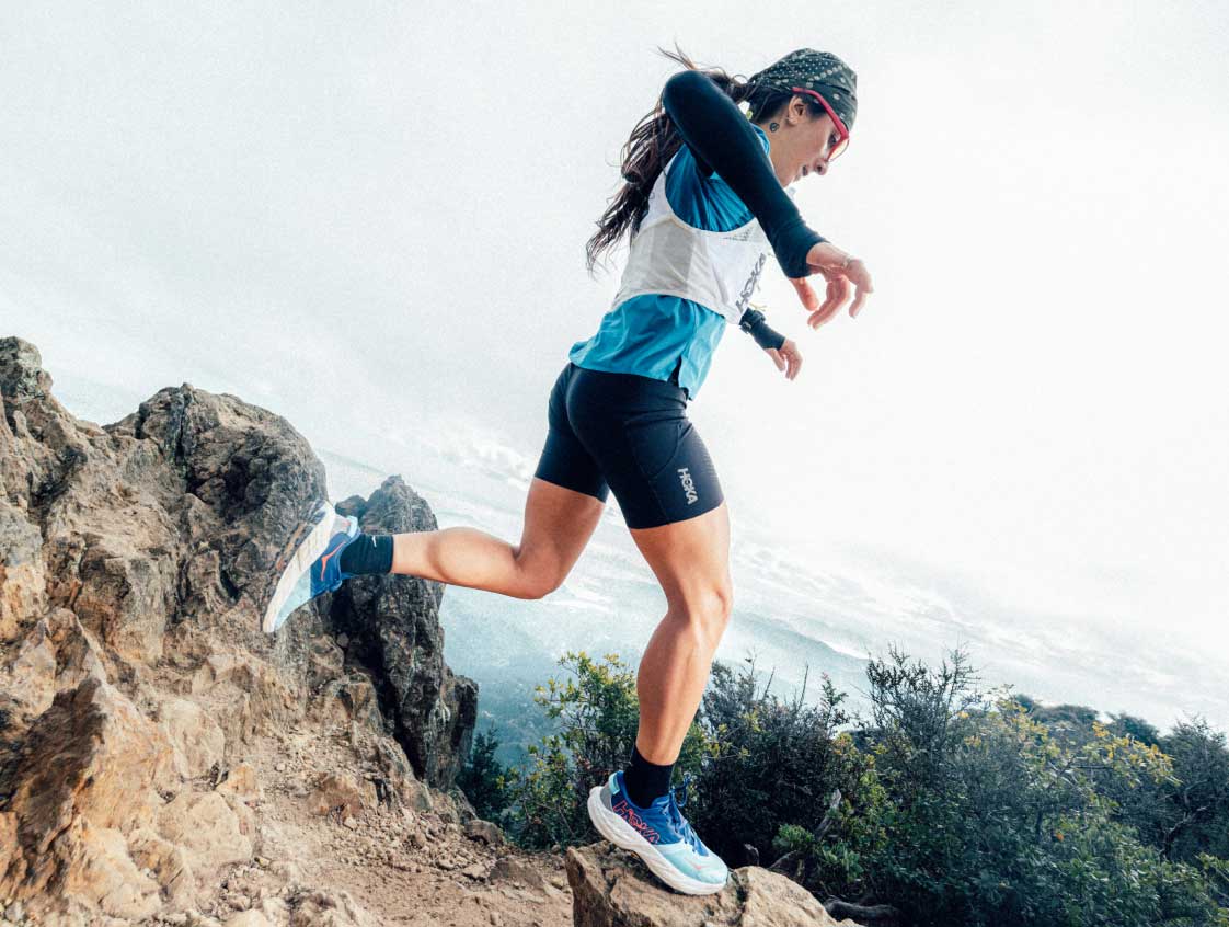 Coureur de sentier portant un Hoka Speedgoat 7 sautant par-dessus des rochers.