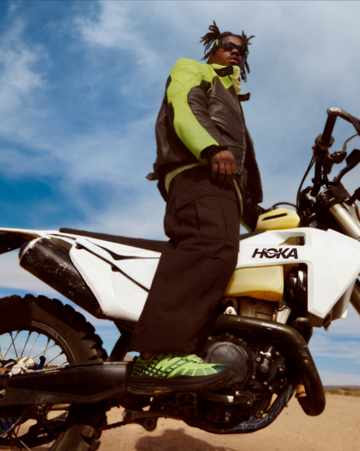 Chaussures HOKA Speedgoat 2 portées alors qu’il était debout sur une moto blanche HOKA.