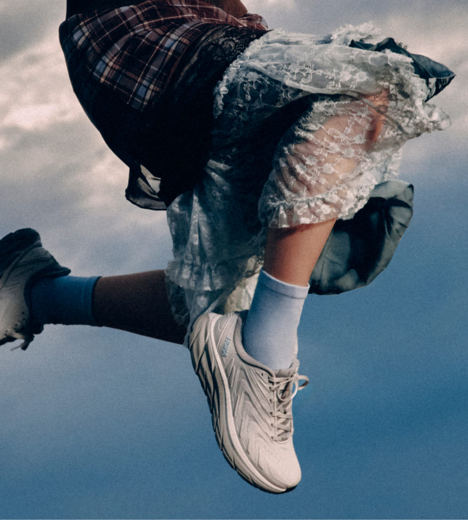 Personne en plein saut sous un ciel nuageux, portant des chaussures HOKA.