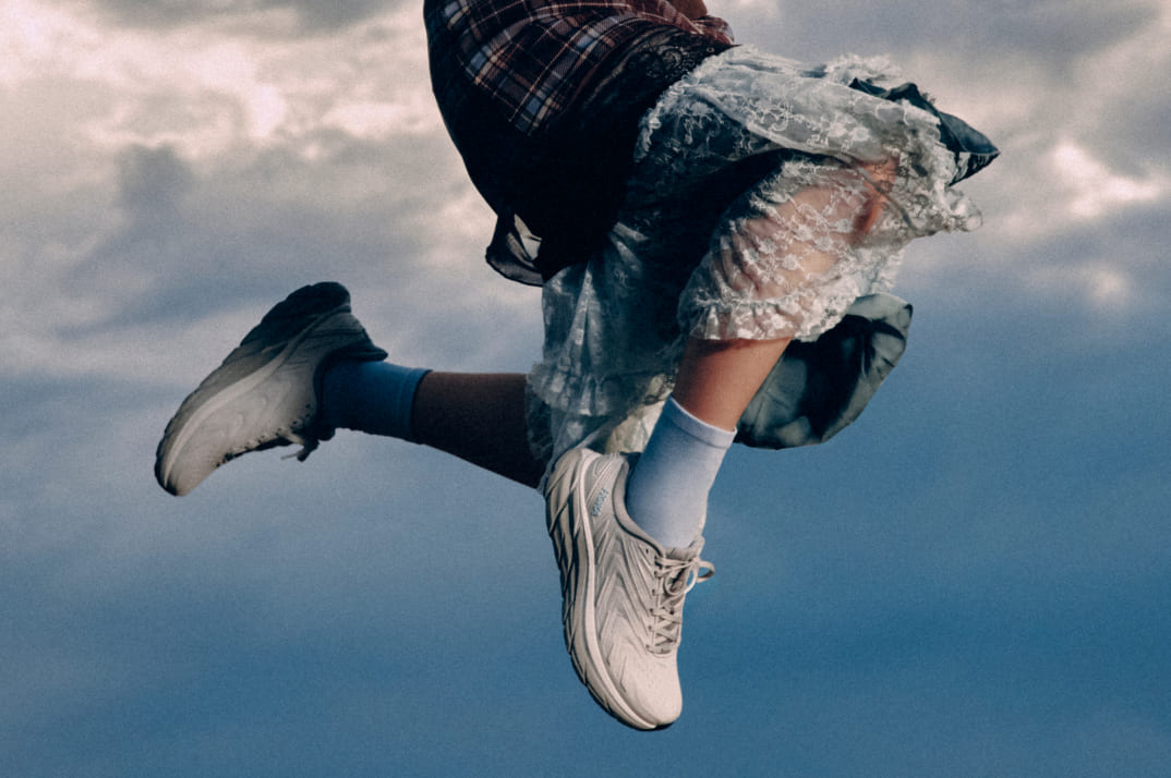 Personne en plein saut sous un ciel nuageux, portant des chaussures HOKA.