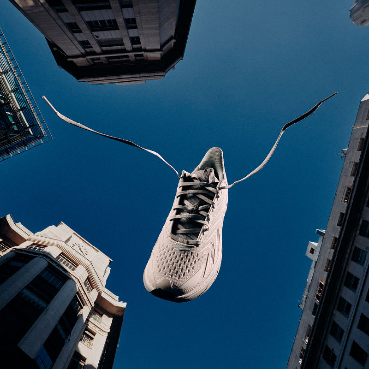 Une chaussure HOKA UTL entre les immeubles de la ville contre un ciel bleu.