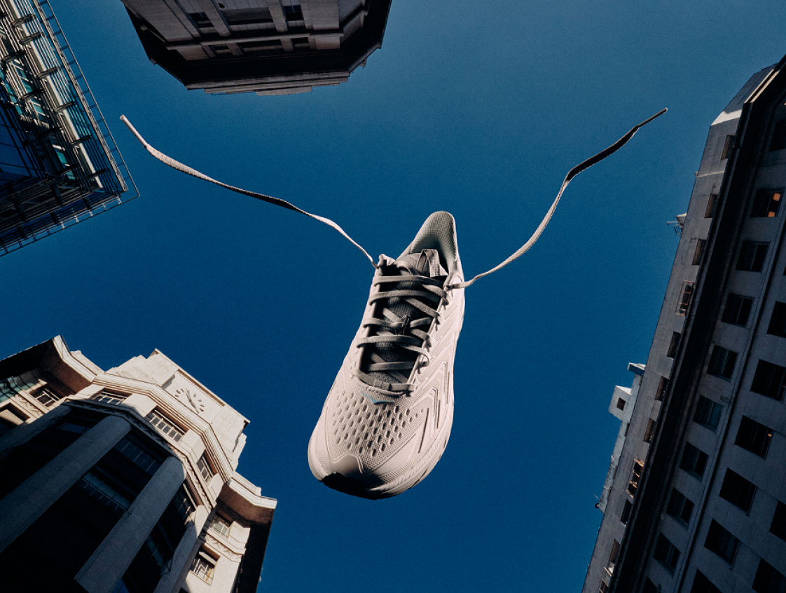 Une chaussure HOKA UTL entre les immeubles de la ville contre un ciel bleu.
