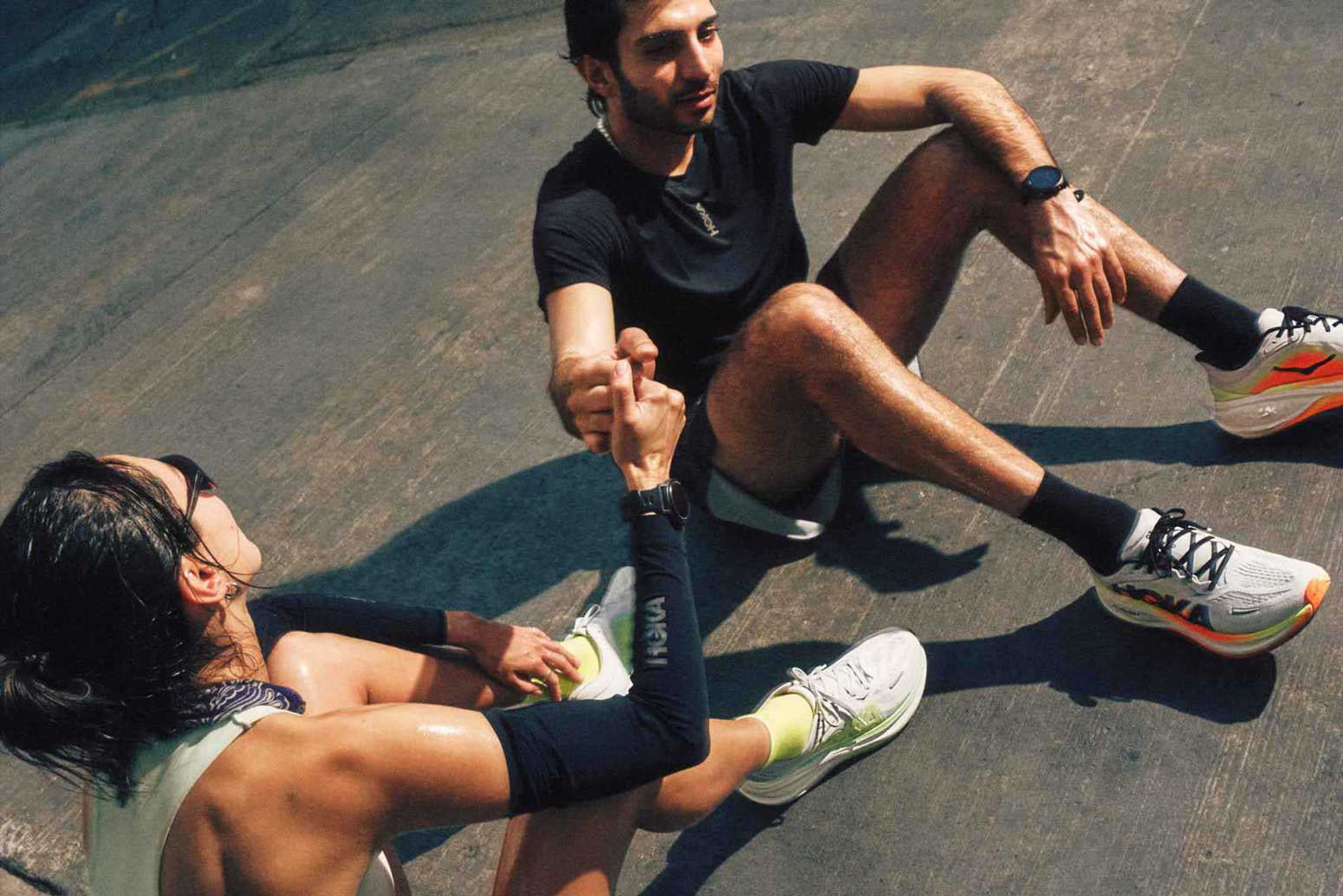 Deux coureurs portant des tenues Hoka, main dans la main, se reposant au sol.