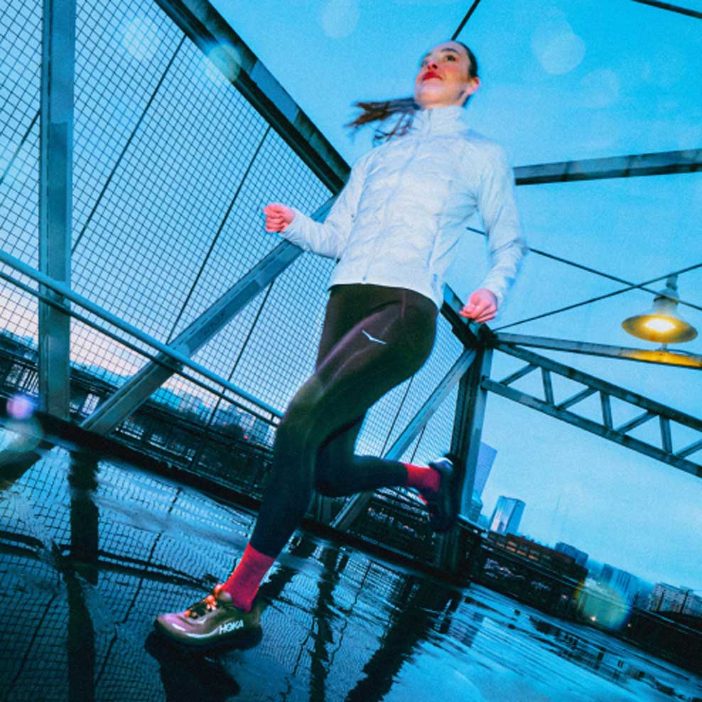 Femme courant sur un pont sous la pluie en portant la Clifton 11 GTX.