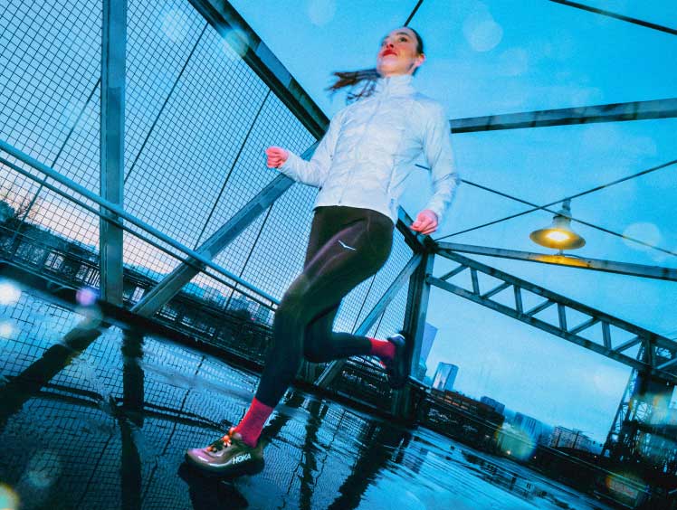 Femme courant sur un pont sous la pluie en portant la Clifton 11 GTX.