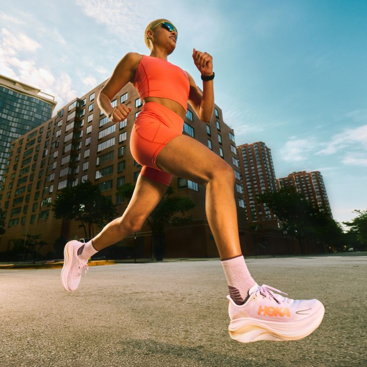 Plan d’action en angle bas d’une femme courant dans une rue de la ville vêtue d’un ensemble de sport orange et de baskets rose pâle.