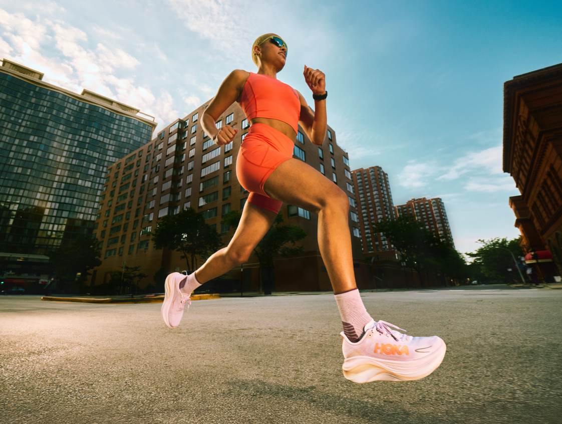 Plan d’action en angle bas d’une femme courant dans une rue de la ville vêtue d’un ensemble de sport orange et de baskets rose pâle.