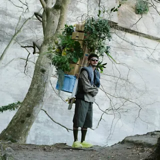 A person standing on a trail while carrying a backpack with supplies and wearing 'HOKA Mafate Three2 Grid JP'